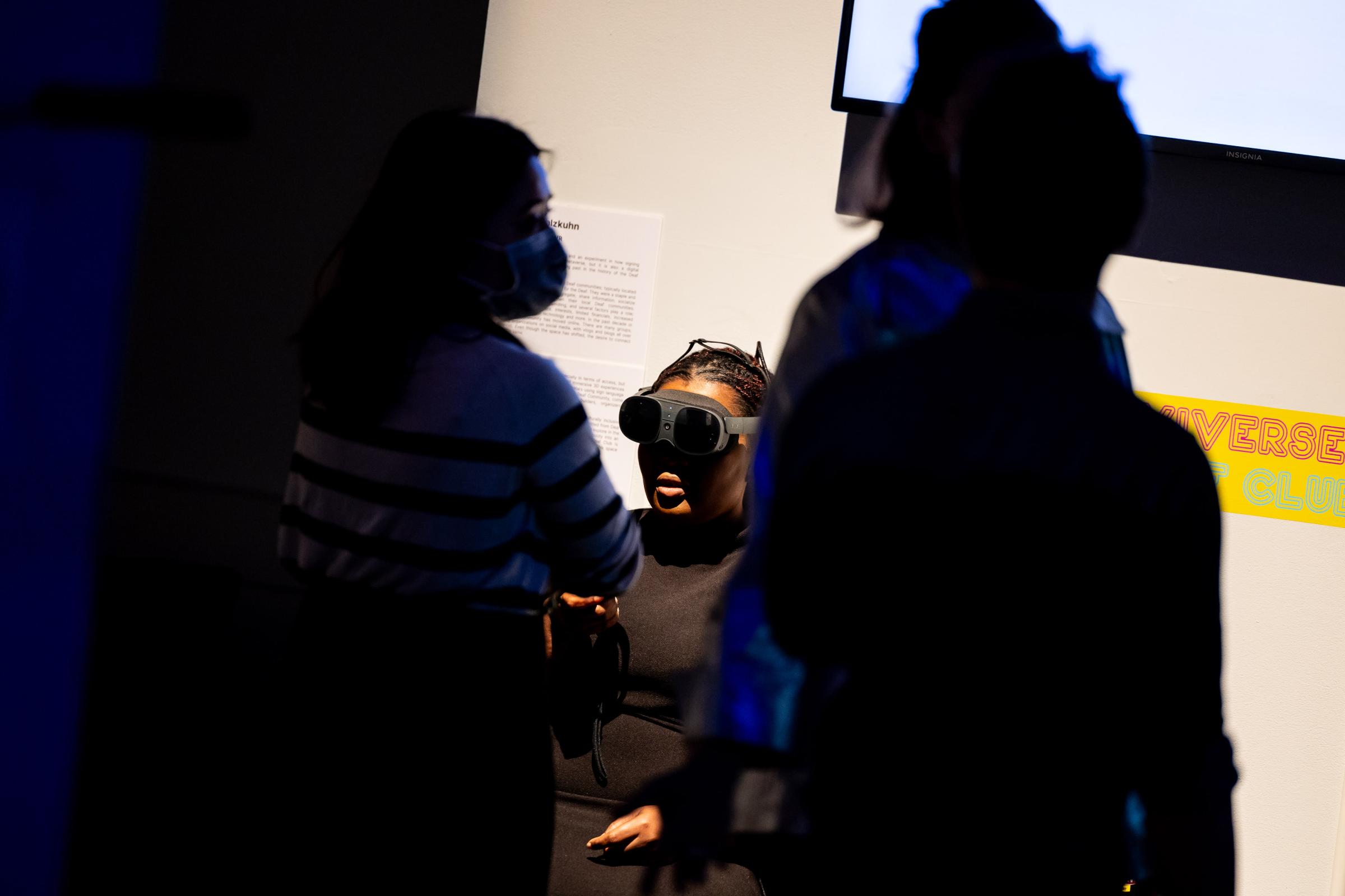 Individual seated with wearing a VR headset in the background while attendees are walking in front. 