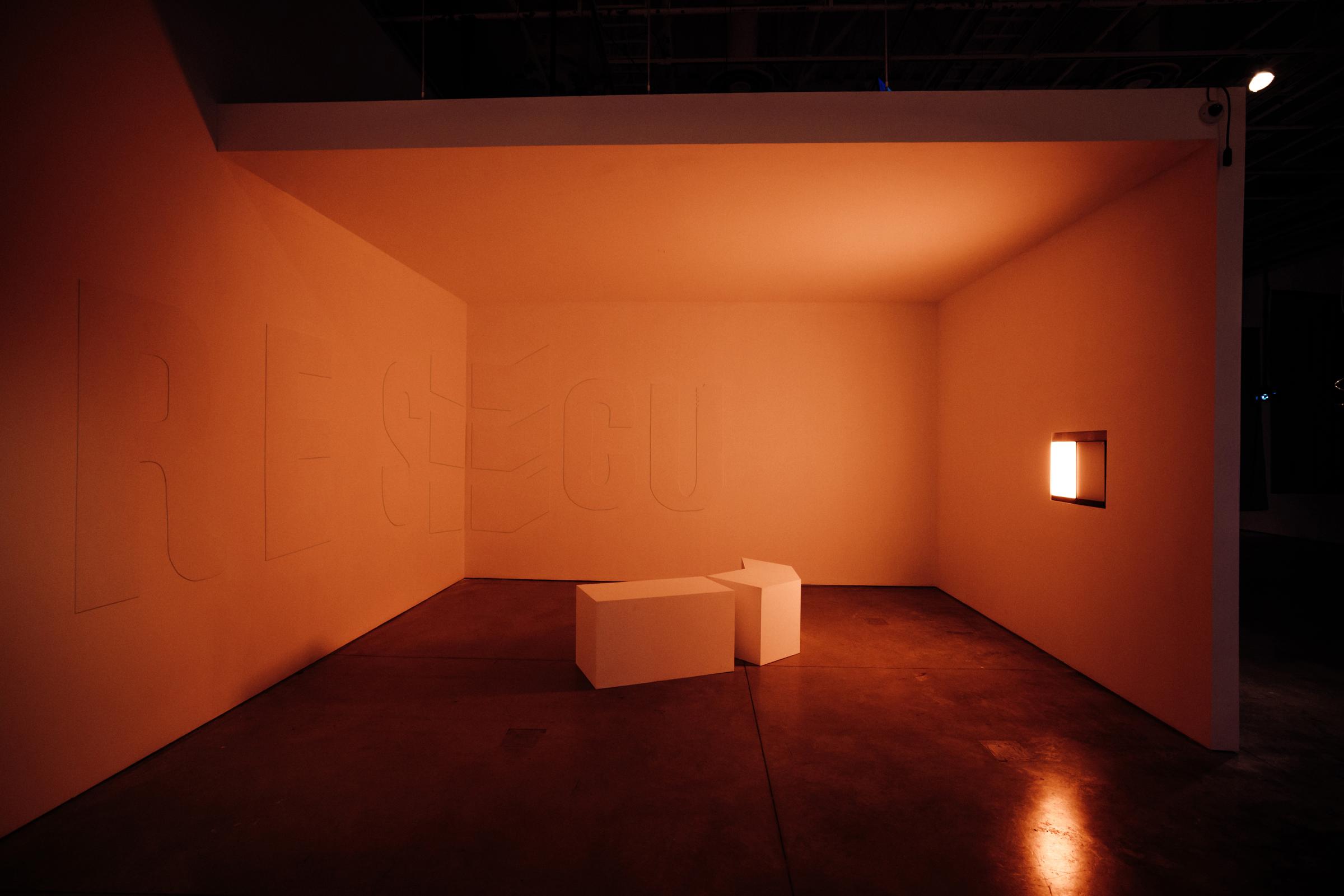 Three walls frame two white stools in the center. On the rightmost wall, a deep orange light source colors the room a rich goldenrod.
