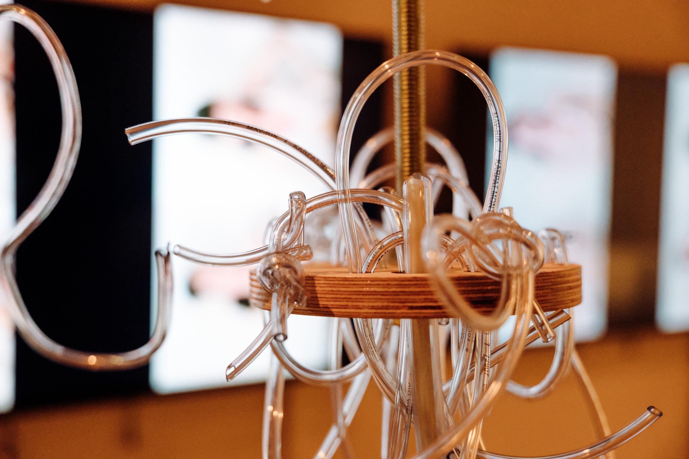 Wooden disk with tubes hanging off of it. A metal rod passes through the middle. In the background, blurred, are two monitors with a human figure.