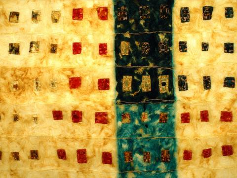 An abstract artwork featuring a grid of small red, gold, and dark blue squares arranged on a textured golden-yellow surface. A central vertical band of deep blue divides the composition, evoking woven fabric or dyed textile.
